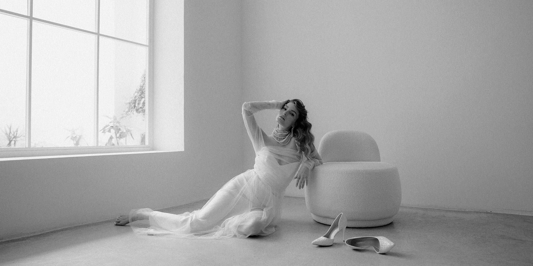 Novia tumbada en el suelo, apoyada en un sillón y con los zapatos quitados, en un momento relajado y despreocupado.