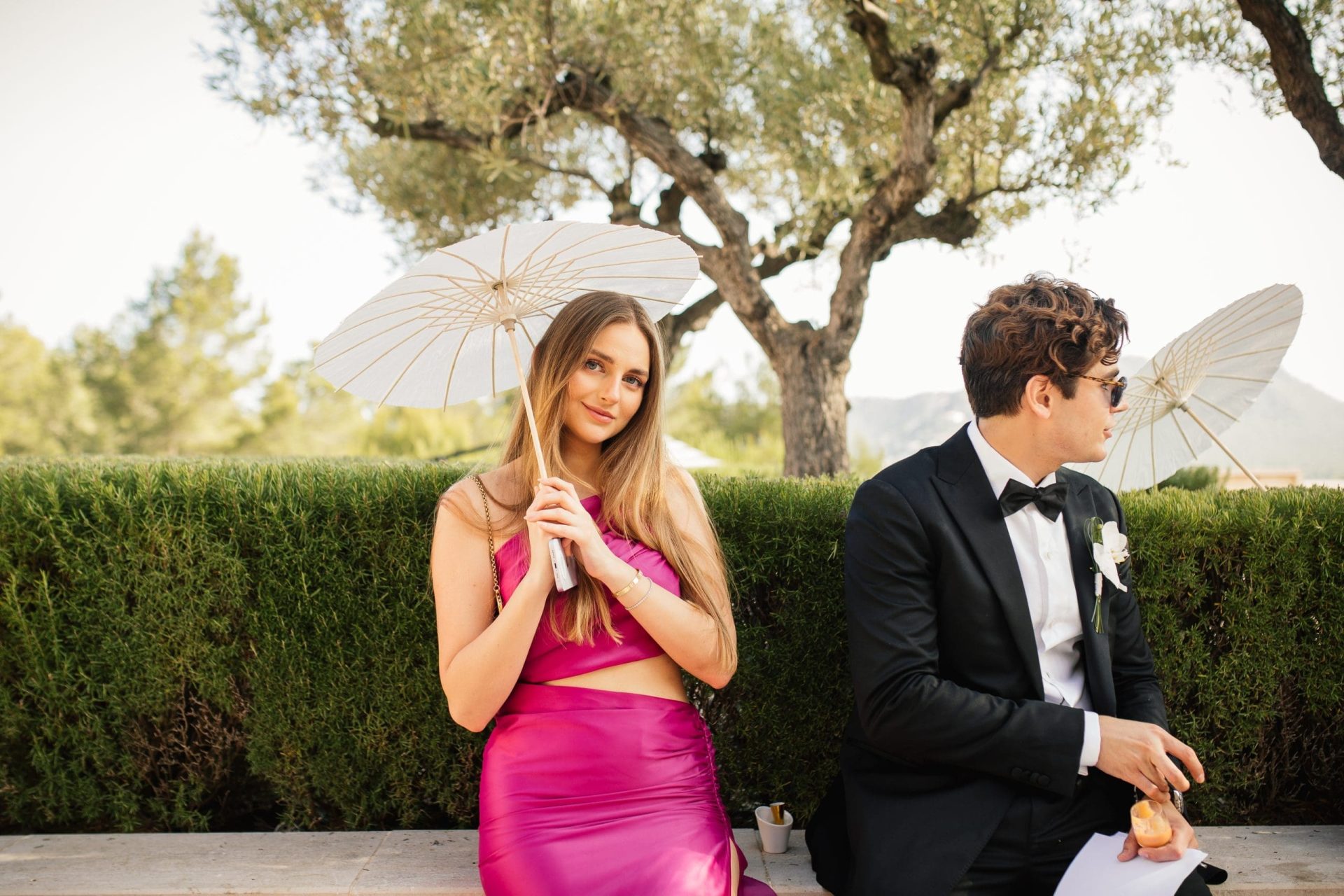 Invitada y padrino con sombrillas en una boda en Cap Vermell Grand Hotel, Mallorca.