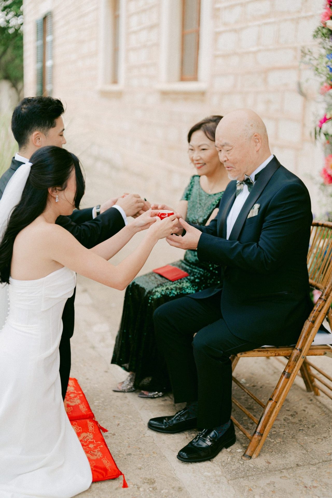 Novios arrodillados ofreciendo vasos de té a los padres de la novia durante la ceremonia del té en una boda china.