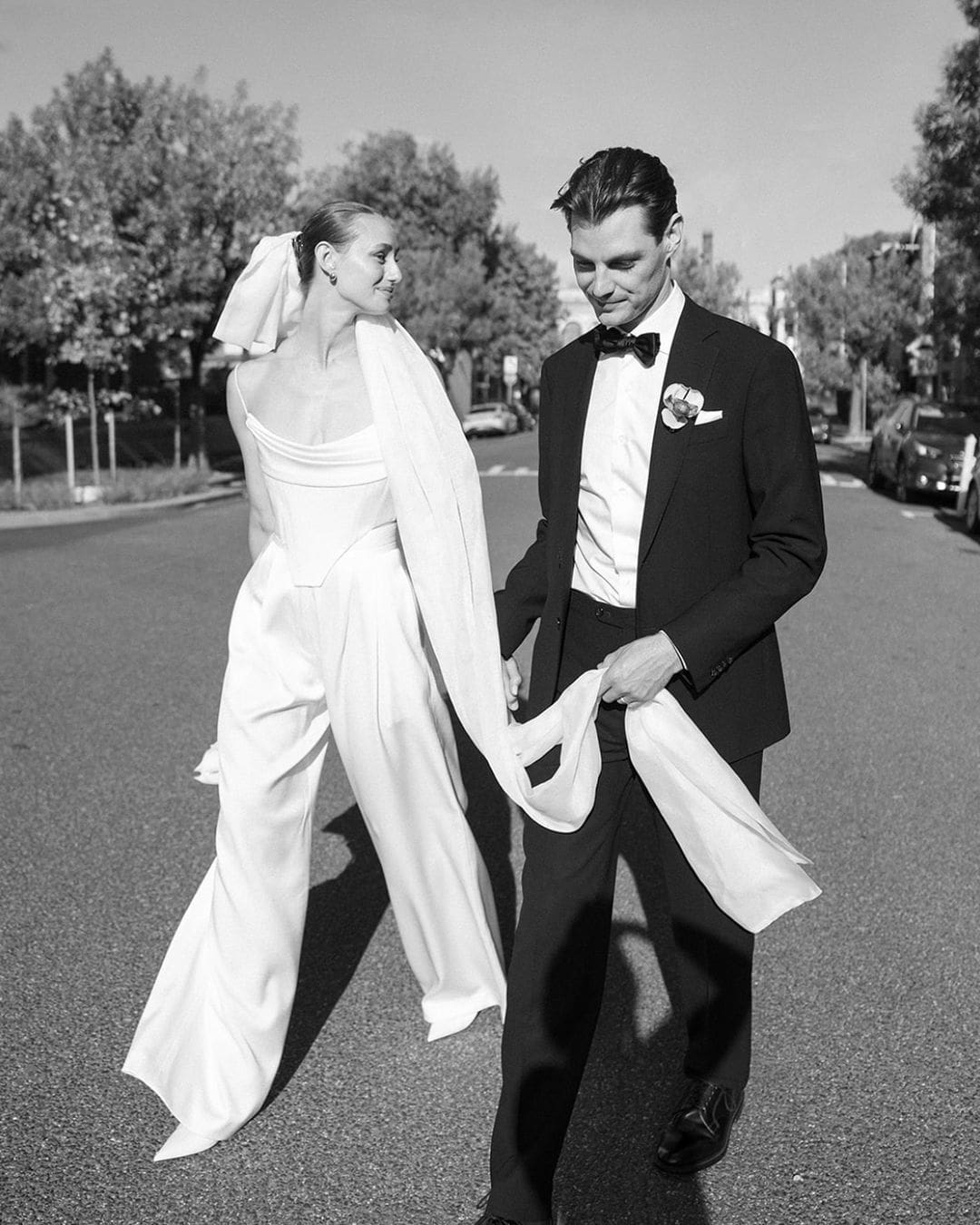 Novia y novio caminando juntos por la calle en fotos de boda, ambos lucen sonrientes y relajados.