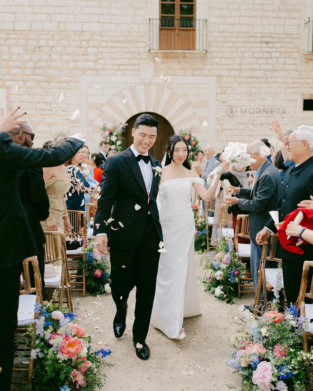 Recién casados caminando entre los invitados mientras lanzan pétalos, destacando cuánto cuesta una boda con decoración floral y ceremonia al aire libre.
