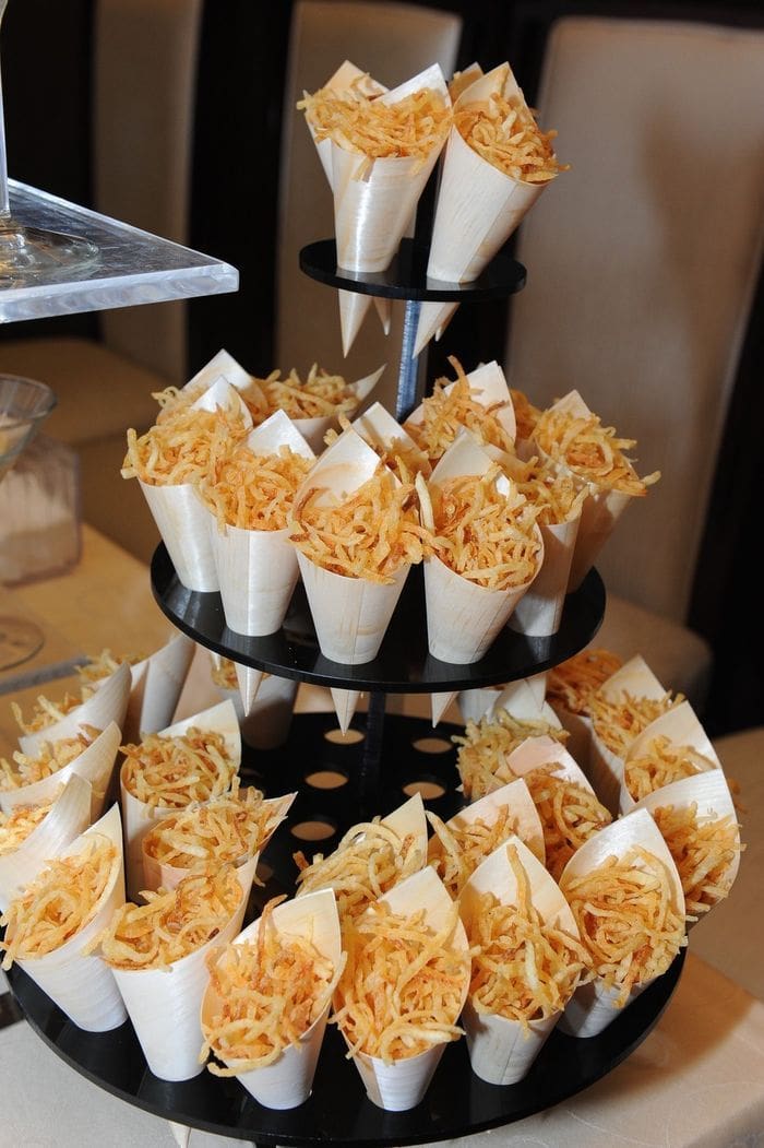 Conos de patatas fritas crujientes servidos en un soporte, una opción salada para la recena de boda.