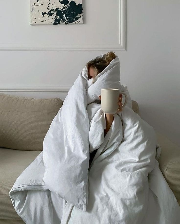 Mujer envuelta en una manta sujetando una taza de café, transmitiendo necesidad de descanso emocional