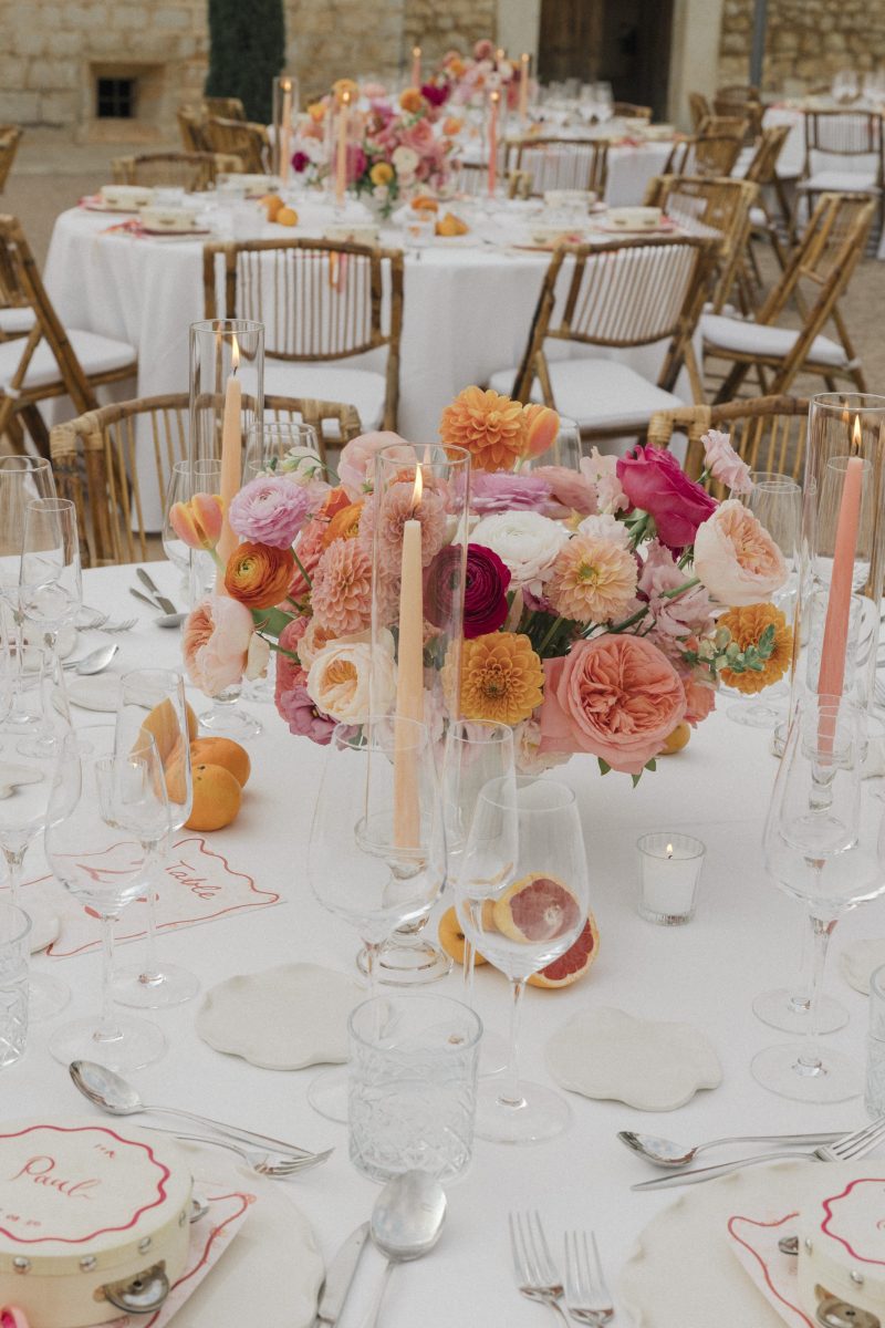 A table centrepiece of roses and dahlias in pink and orange, with coloured tapers, at Adele and Ian's wedding at Finca Morneta