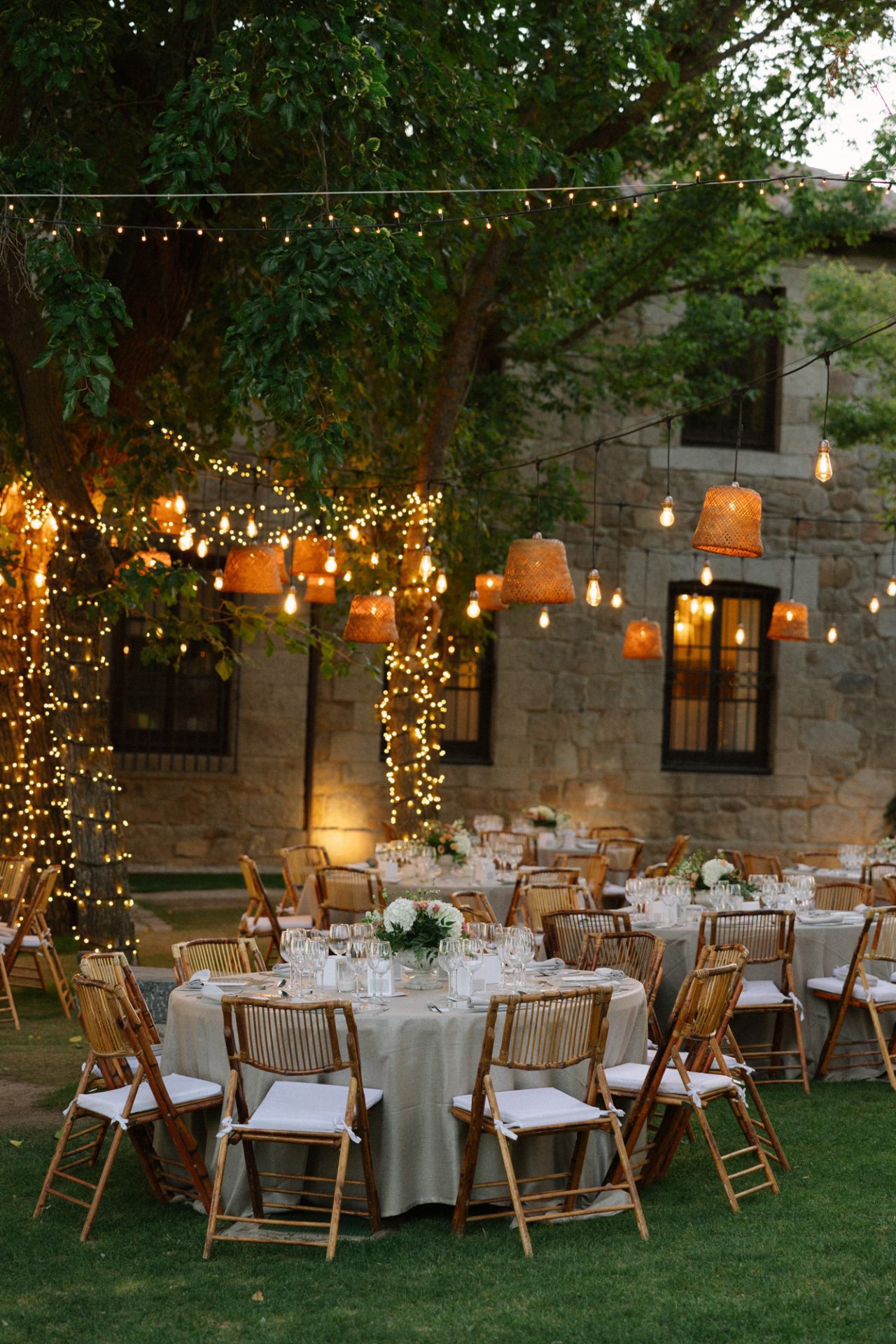 Mesas montadas en el jardín de la Finca El Gasco bajo guirnaldas de luces, en la boda de Cynthia y Sara