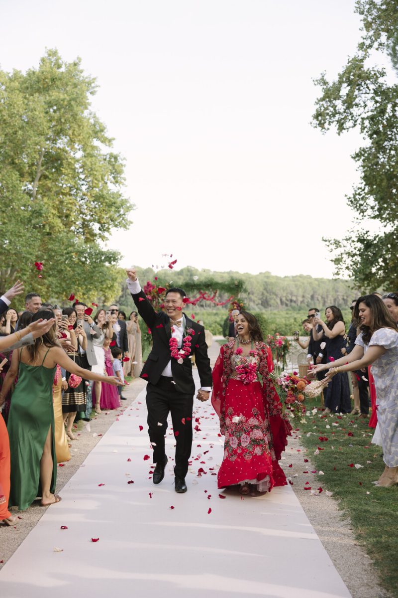 Hema and John walk out through red petals after their Indian wedding at Vallesa de Mandor, Valencia