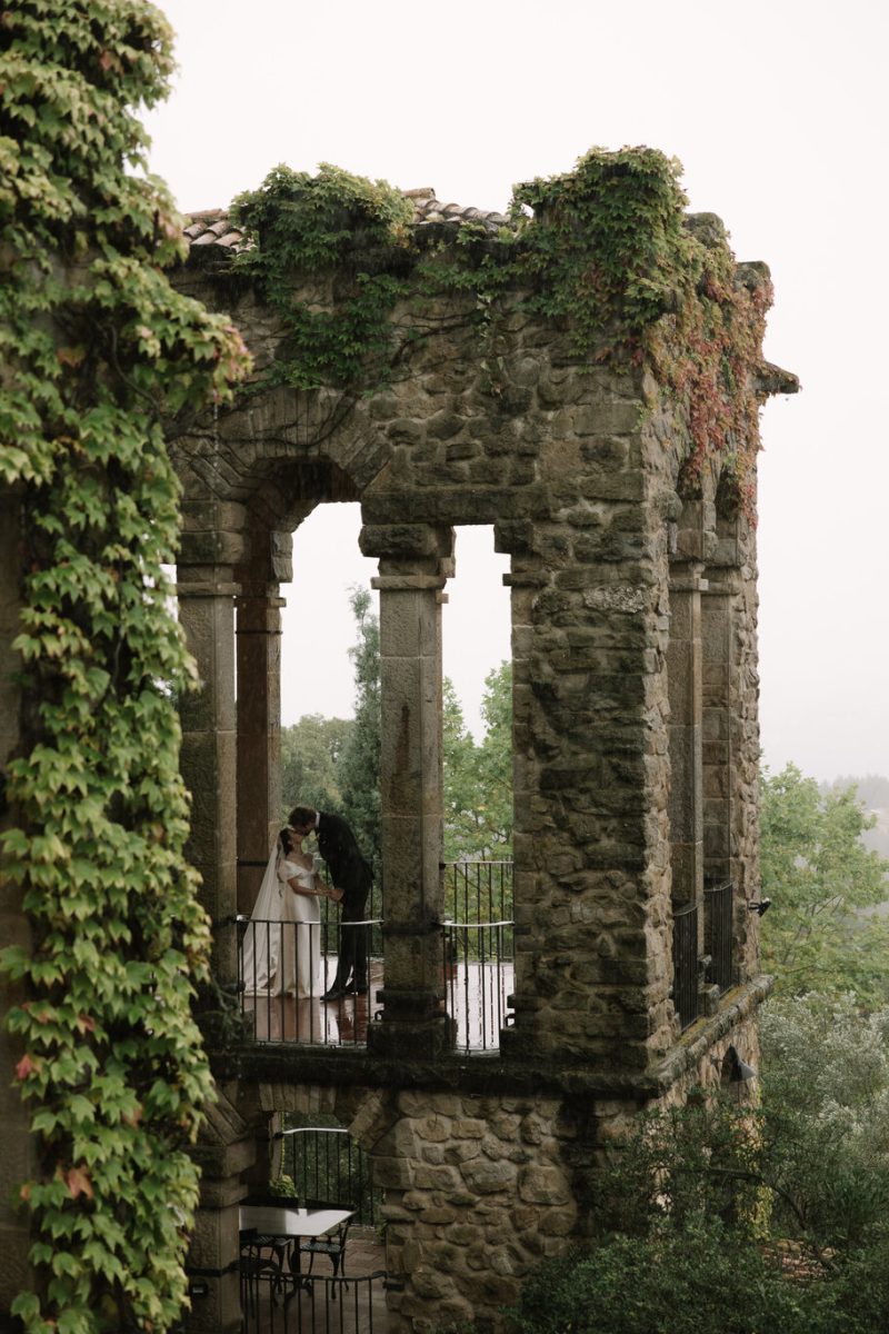 Abbie and Norman kissing in the ivy-covered stone gallery at La Baronía, near Barcelona