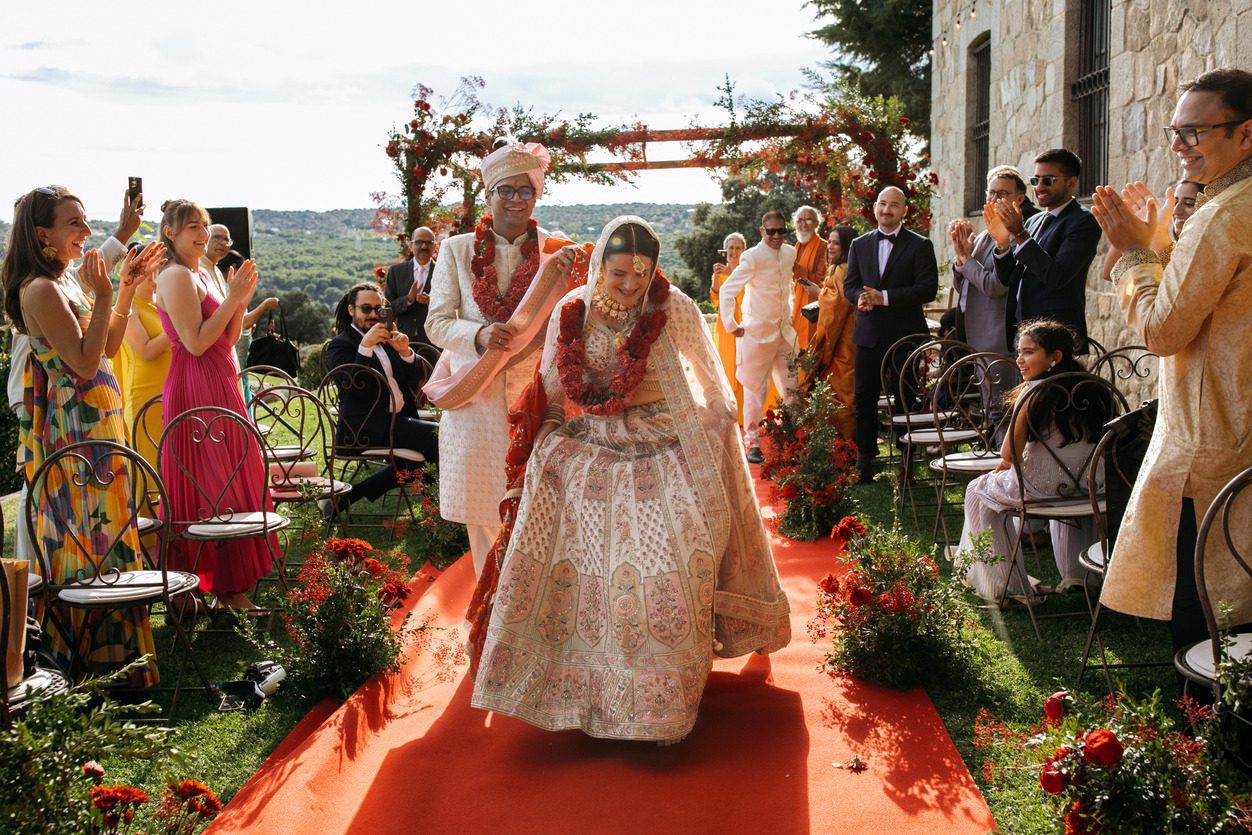 The bride walking to the mandap at an Indian wedding in Spain, with the family on both sides