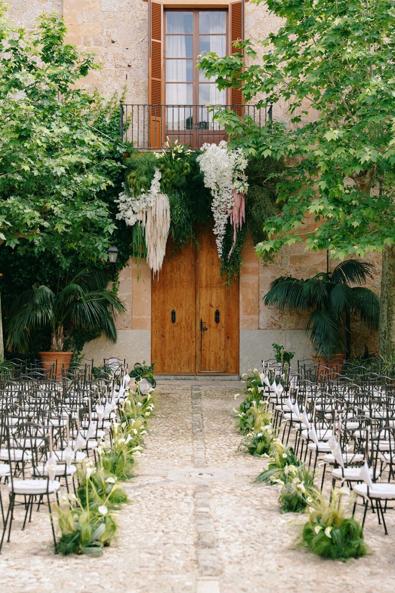 Pasillo de la ceremonia con sillas y plantas hasta la puerta de madera de Son Togores, en Mallorca